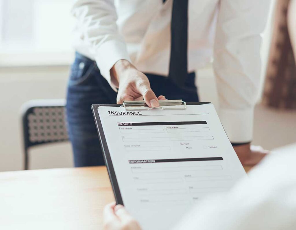 A couple reviews auto and home insurance documents beside a laptop and calculator at a kitchen table.
